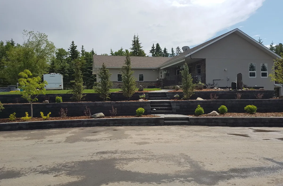 Newly planted trees and multi-coloured bushes among tiered Keystone retaining walls in front of home